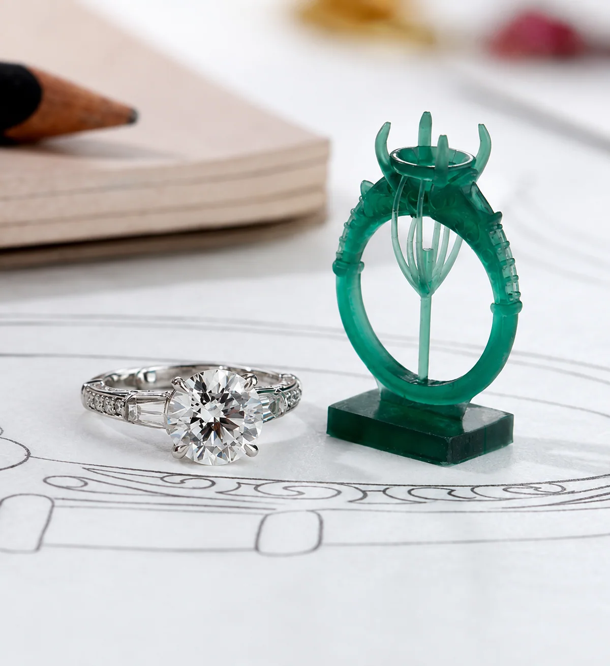 Finished platinum solitaire beside its green wax casting model, resting on the design sketch