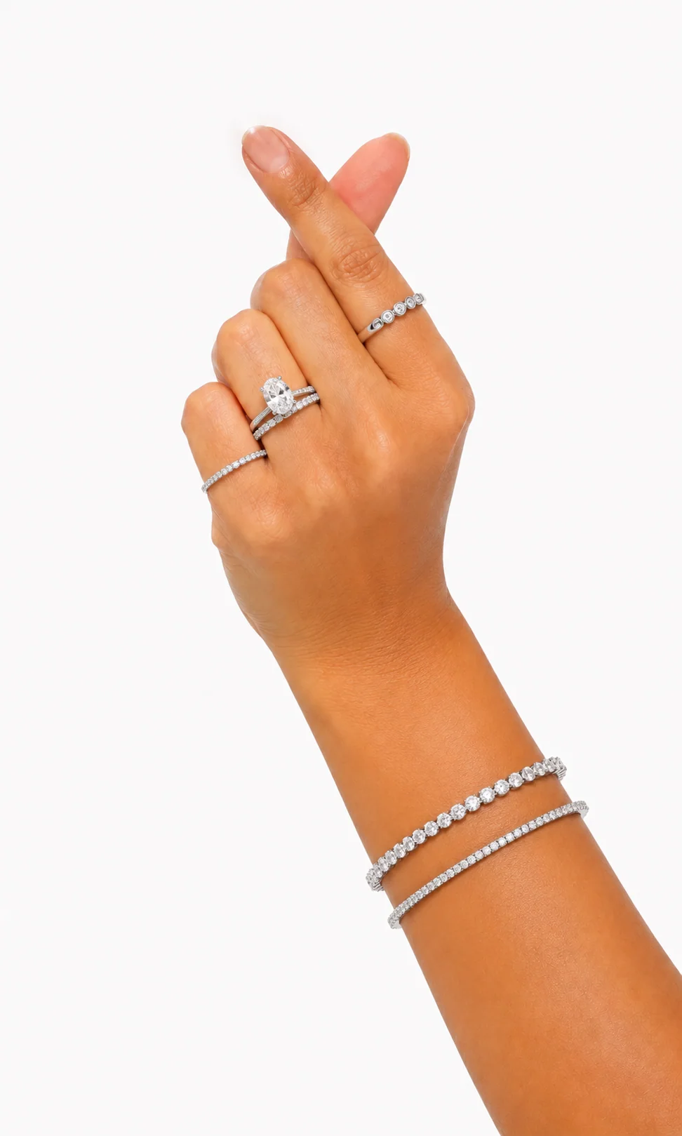 Hand wearing an oval diamond solitaire, pavé bands, and two tennis bracelets