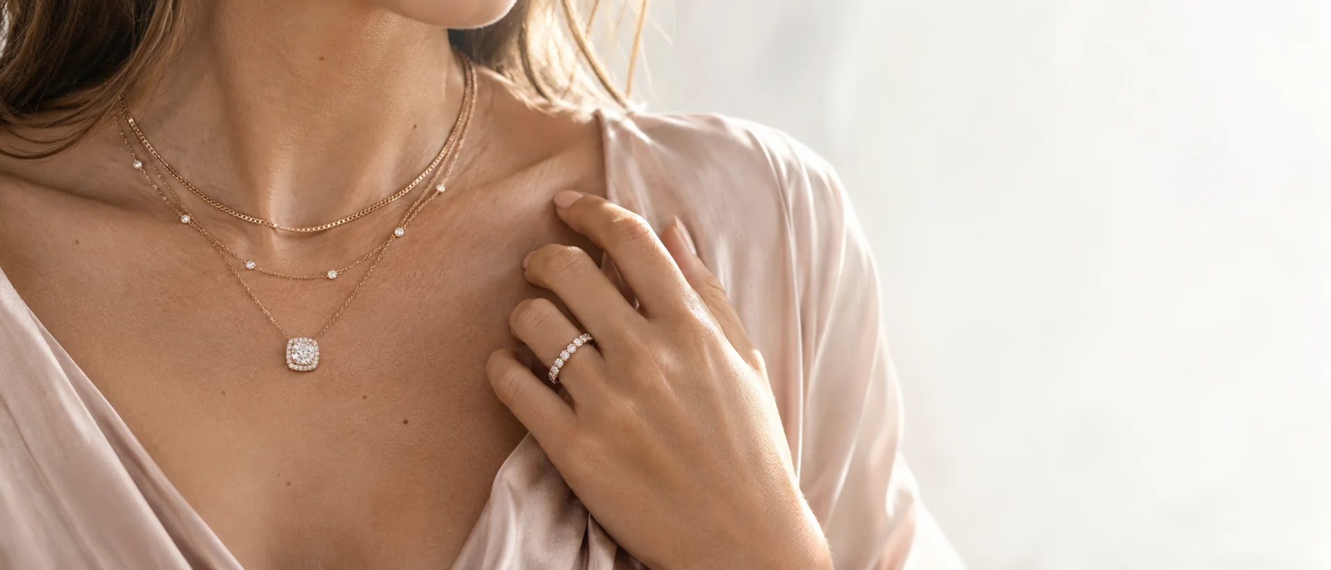 Three fine layered necklaces with a diamond halo pendant, a hand with a diamond eternity band resting at the collarbone