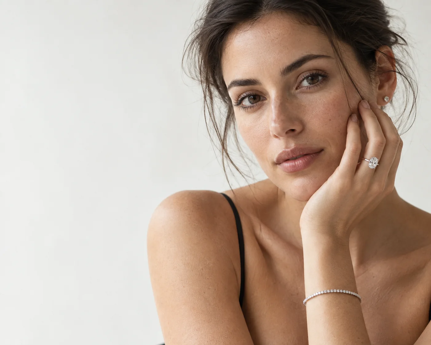 Woman with dark hair resting her cheek on her hand, wearing an oval diamond solitaire, a diamond stud and a tennis bracelet