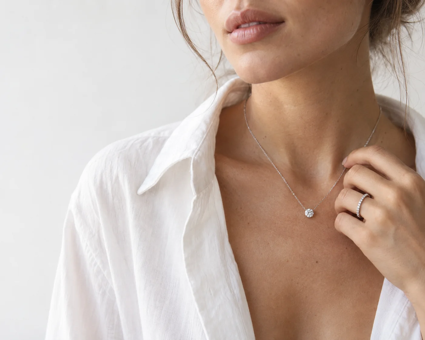 Open white shirt and a round diamond pendant at the collarbone, a pavé diamond band on her hand