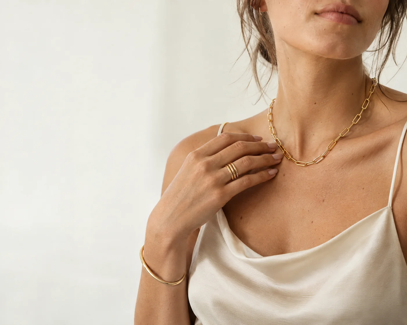 Ivory silk slip, a gold paperclip-link necklace, stacked gold bands and a gold bangle